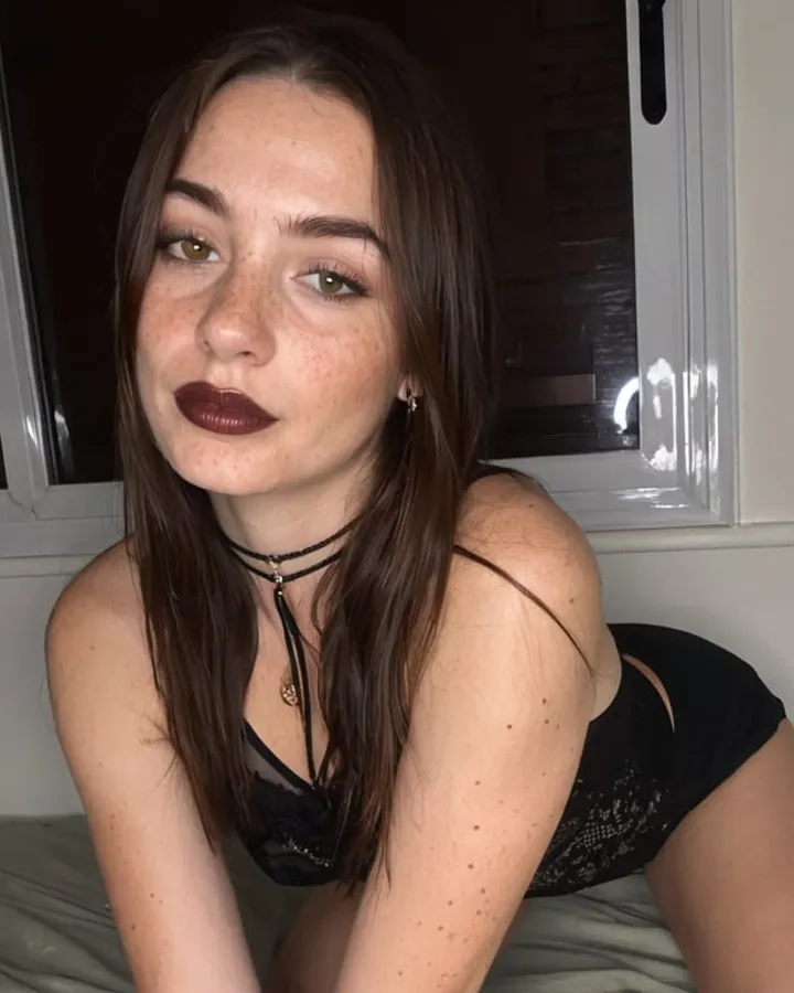 Compañera IA con pecas y labios oscuros junto a una ventana, de Dondi AI